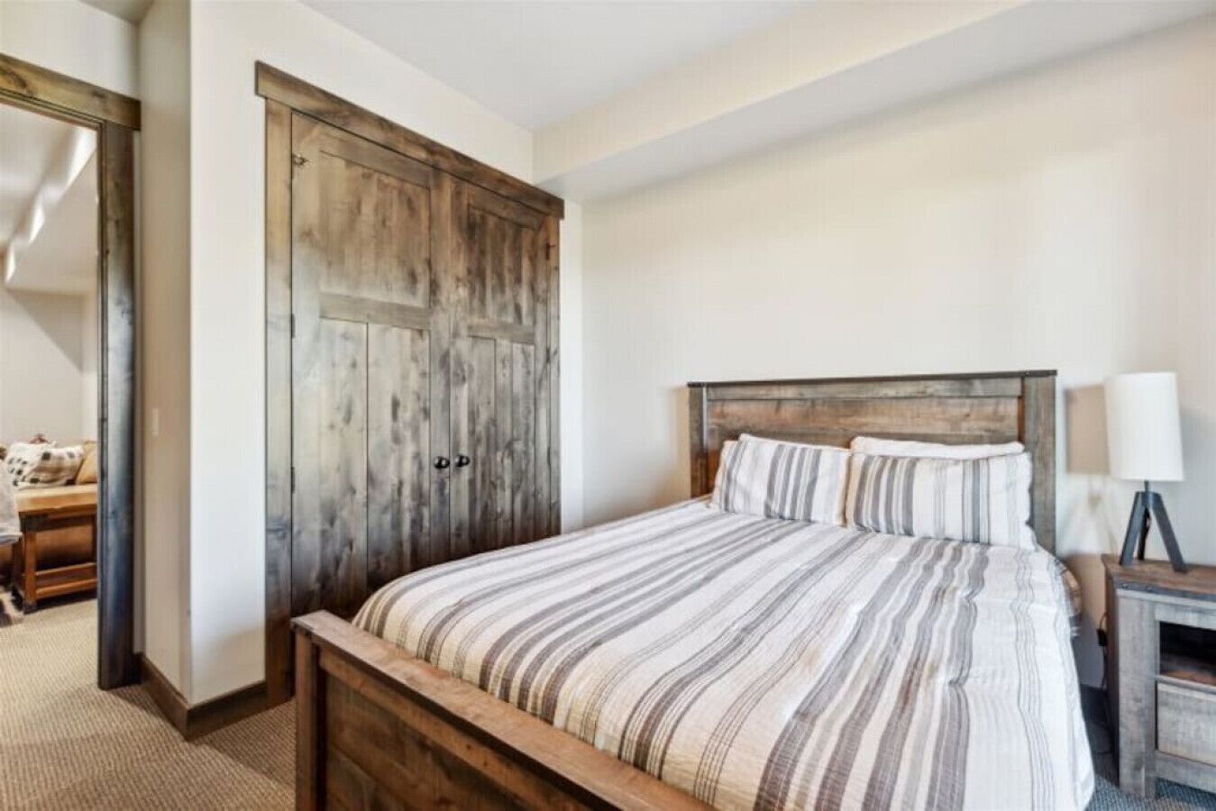 A bedroom with a wooden bed frame, striped bedding, and a wooden wardrobe.