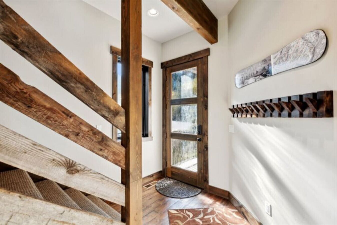 Eine Holztreppe führt zu einer Tür mit Fensterteil, auf dem Boden liegt ein gemustertes Teppich und an der Wand hängt ein dekoratives Element.