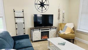 A living room with a sofa, a coffee table, a TV, a fireplace, and a decorative wall piece. - Ocean Views New 4BR Steps from Beach (Myrtle Beach)