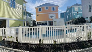 A pool area with a white fence, surrounded by colorful houses. - Ocean Views New 4BR Steps from Beach (Myrtle Beach)
