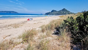 A beach with a tent and a beach umbrella, sandy terrain, and a distant mountain. - Roberts Beach Escape in Tairua is 3-5 minute walk from the beach (Tairua)