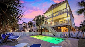 A two-story building with a pool, lounge chairs, and a white picket fence.
