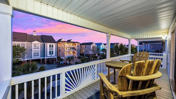 A covered deck with wooden chairs and a view of residential buildings.