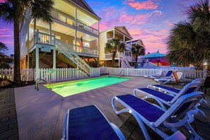 A beachfront hotel with a pool, lounge chairs, and a white picket fence. - 5BR Beach Views w/ Pool | Walk to Pier and Beach (Surfside Beach)