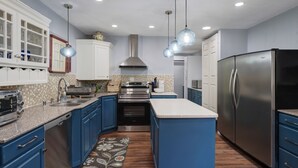 A modern kitchen with blue cabinets, stainless steel appliances, and pendant lighting.