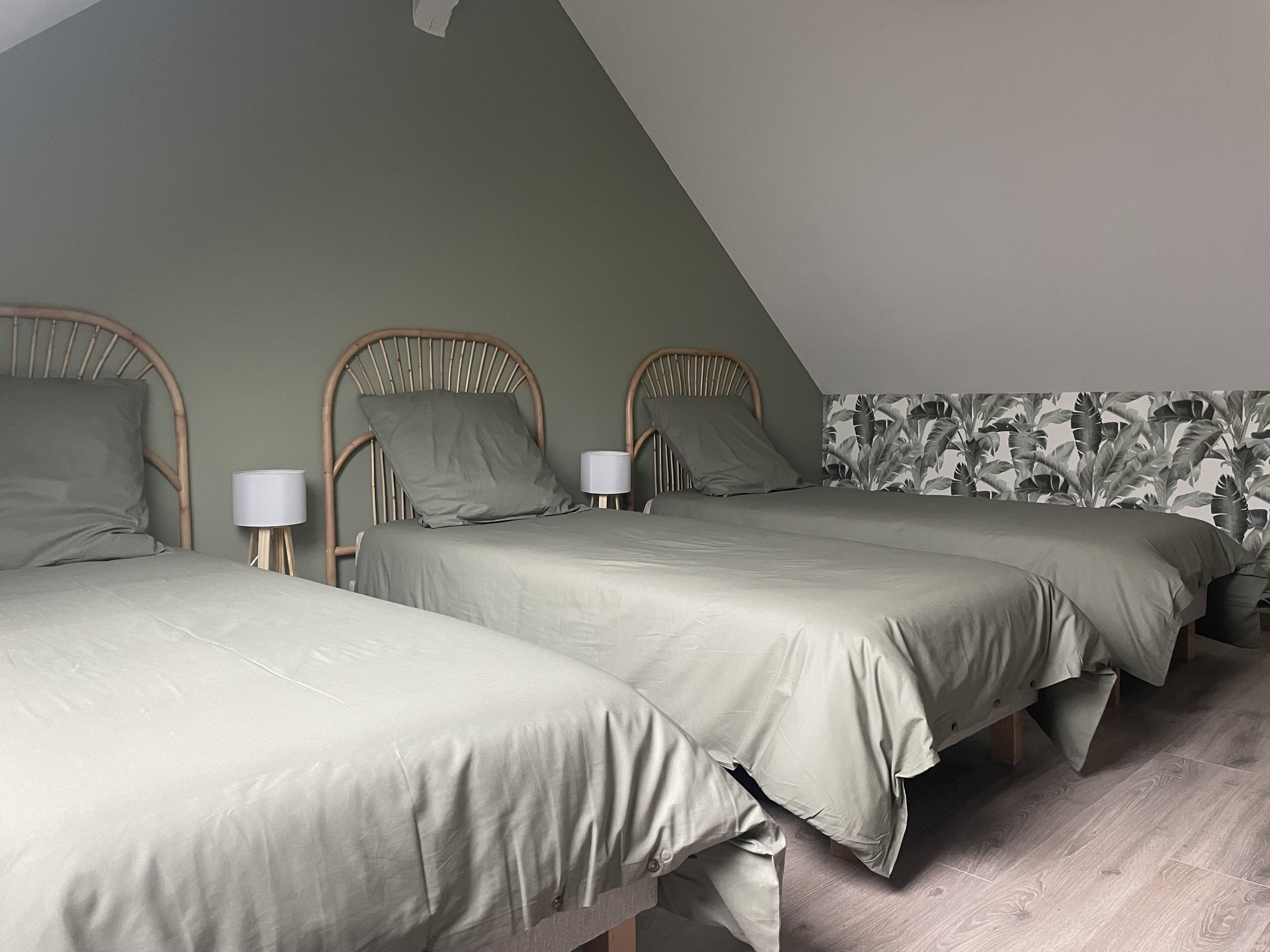 Een slaapkamer met twee eenpersoonsbedden, een houten hoofdbord, een nachtkastje met lamp, en een wand met een bladmotief.