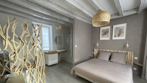 A bedroom with a bed, bedside tables, a mirror, a hanging light fixture, and a shower area.