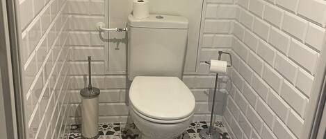 A small, tiled bathroom with a toilet, a toilet paper holder, and a bidet.