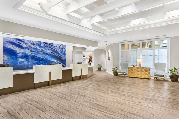 A spacious lobby with a reception desk, a large abstract painting, and a seating area with chairs and a wooden sideboard.