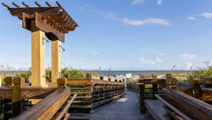 A wooden boardwalk leading to a beach with a wooden pergola structure.