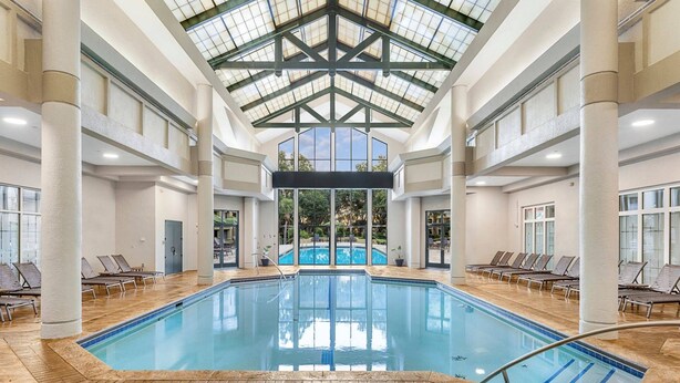 An indoor swimming pool with clear glass ceilings, multiple lounge chairs, and a view of the outdoors.