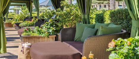 An outdoor seating area with wicker furniture, green cushions, and potted plants.