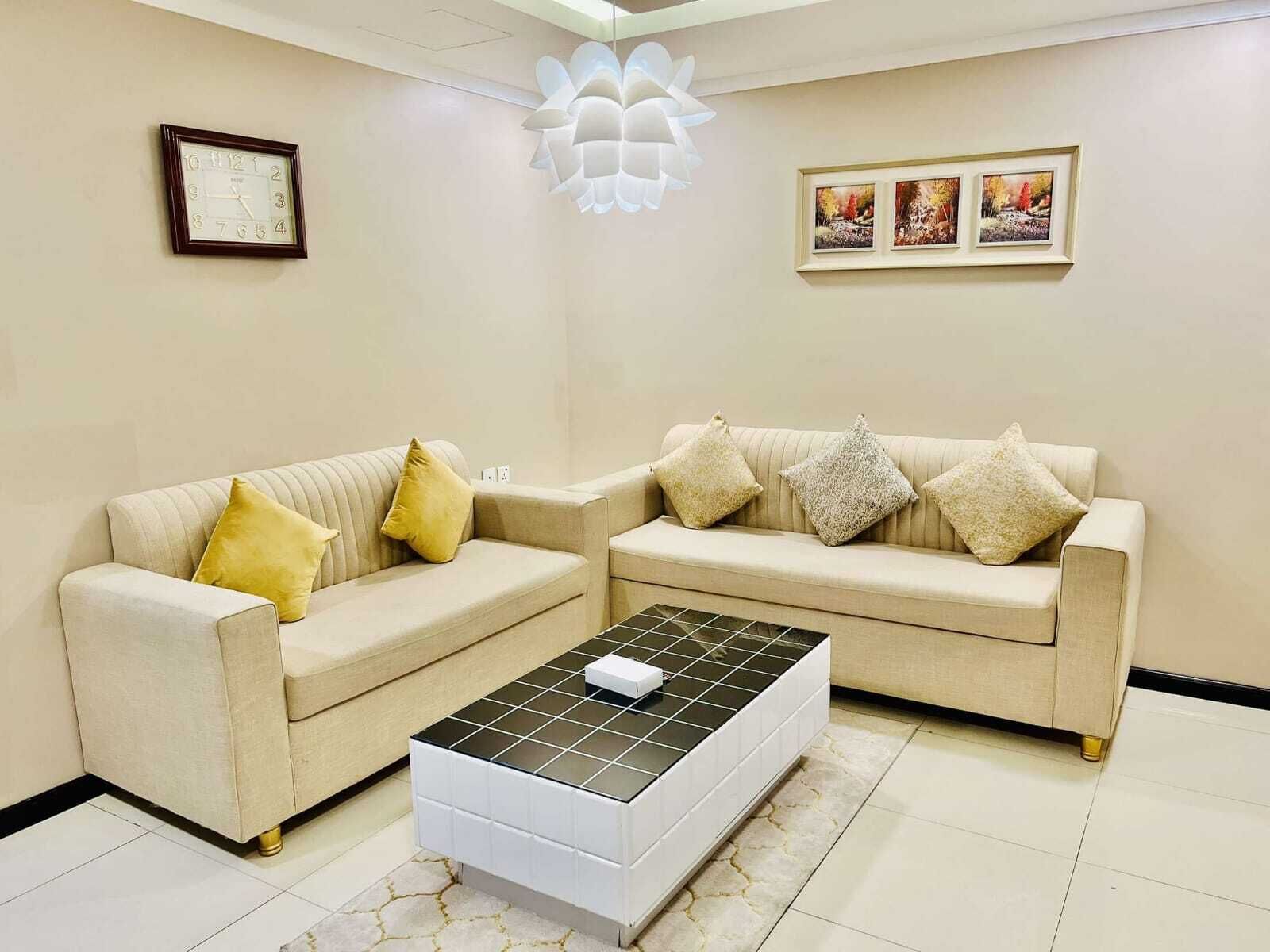 A living room with two beige sofas, a coffee table, a wall clock, and framed pictures.