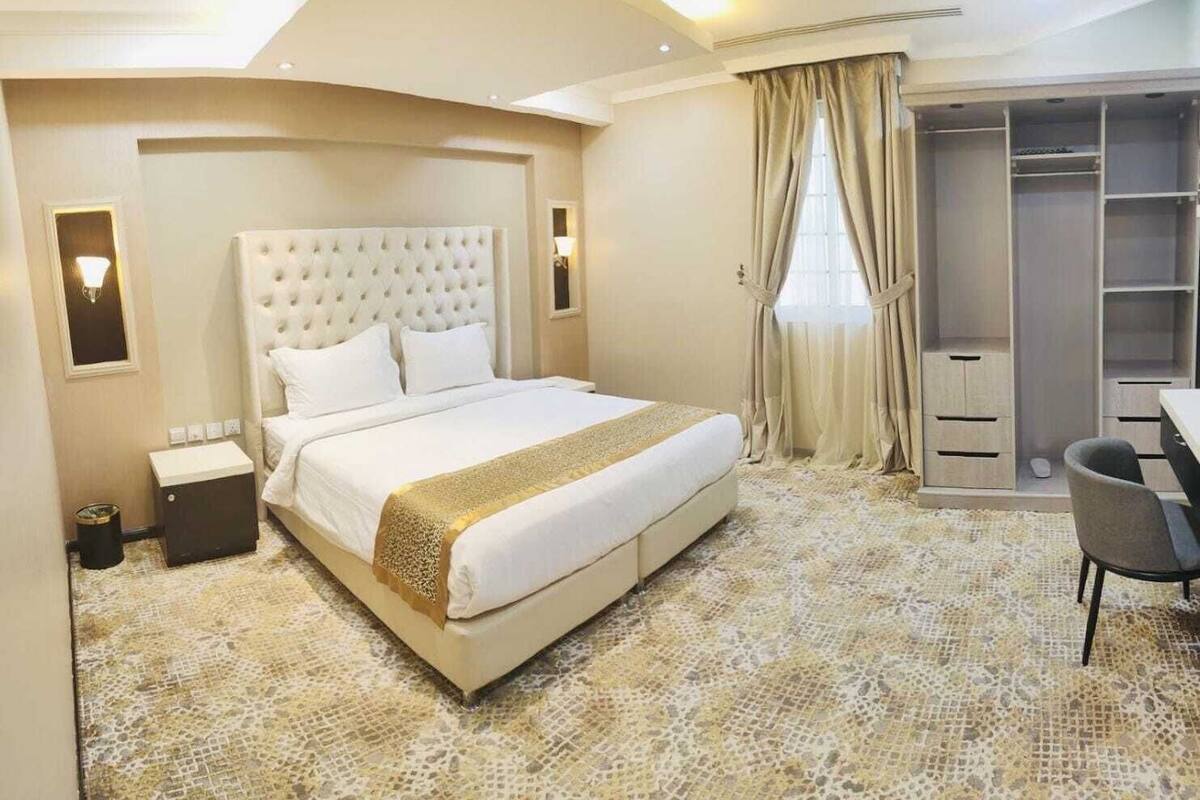 A hotel room with a large bed, a desk, a chair, a wardrobe, and a bathroom.