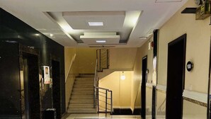 Un hall d’hôtel avec un escalier central, une moquette à motifs et un sol carrelé.