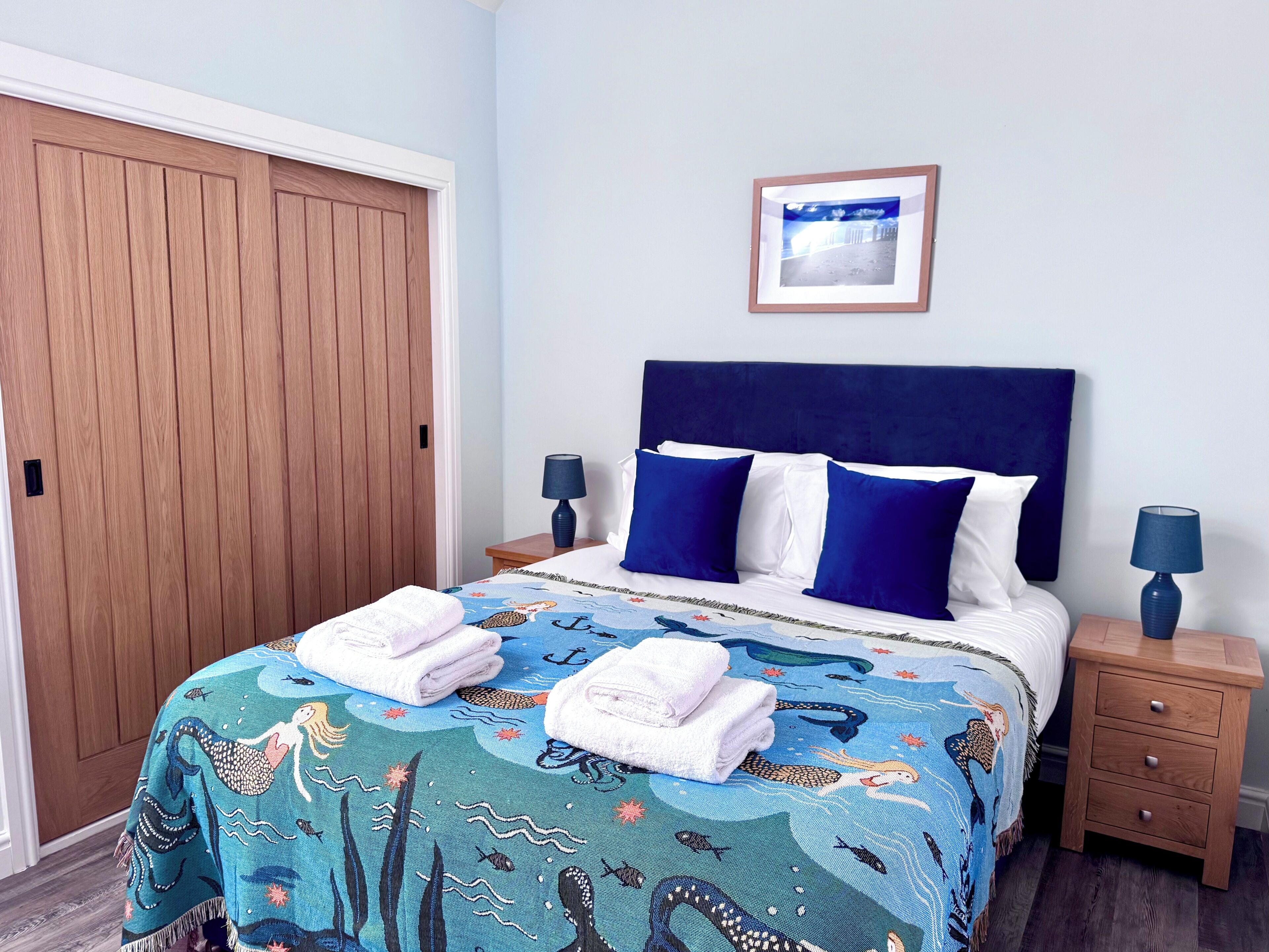 A neatly made bed with a blue and white bedspread, two pillows, and two bedside tables with lamps.