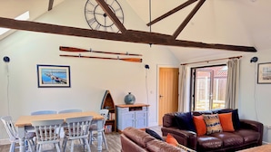 A cozy living room with a brown leather sofa, a wooden dining table with chairs, and a bookshelf. - The Long Barn, Brick Kiln Barns, Dilham - Sleeps 6 in Luxury - Dog Friendly (Dilham)