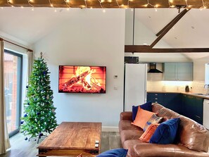 A modern living room with a fireplace, a Christmas tree, and a kitchen in the background.