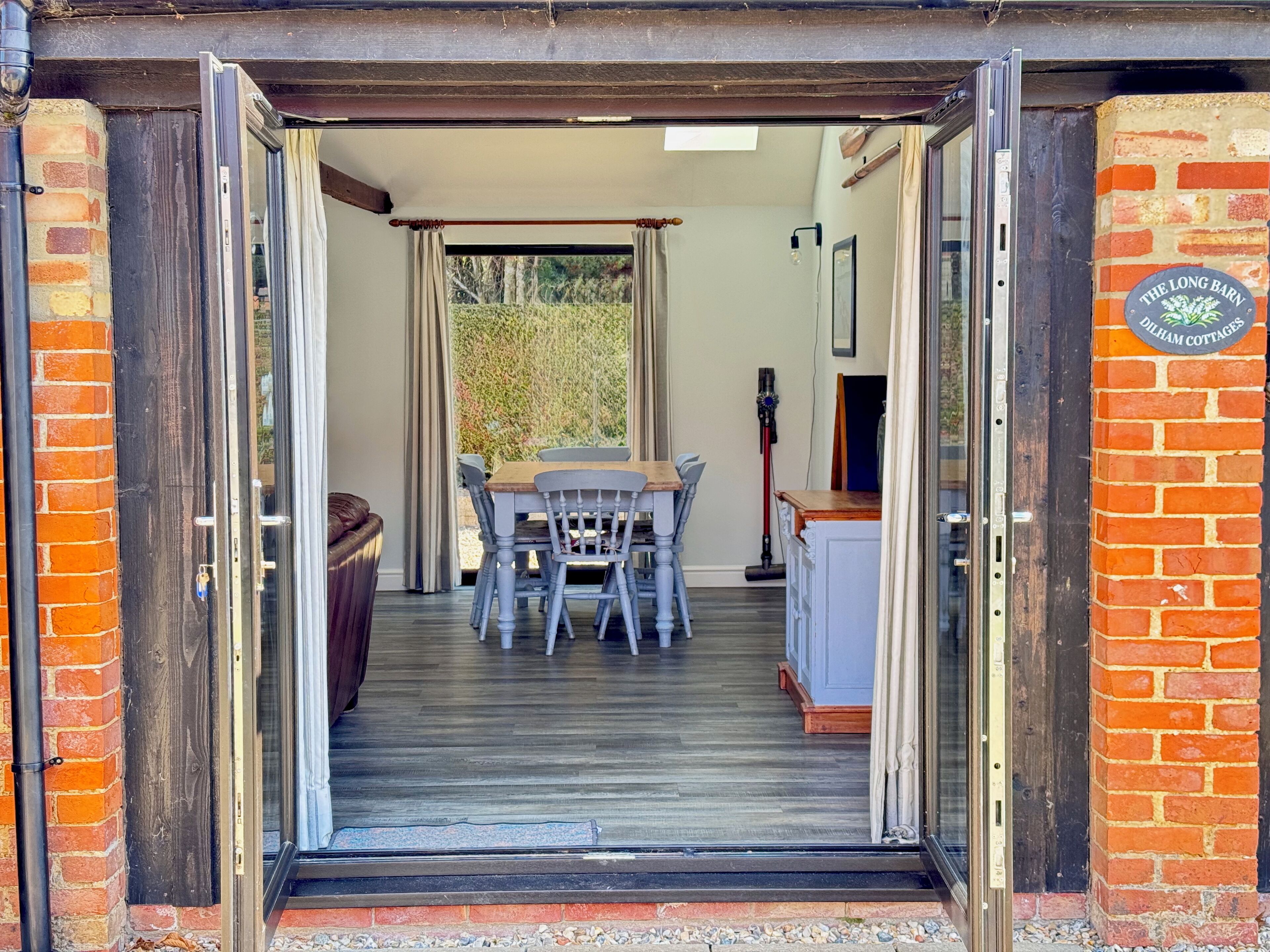 Una puerta abierta que da a un comedor con una mesa y sillas, una pared de ladrillo y un letrero que dice 'The Long Barn'.