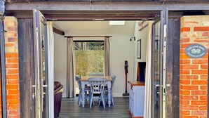 An open doorway leading to a dining area with a table and chairs, a brick wall, and a sign indicating 'The Long Barn'. - The Long Barn, Brick Kiln Barns, Dilham - Sleeps 6 in Luxury - Dog Friendly (Dilham)