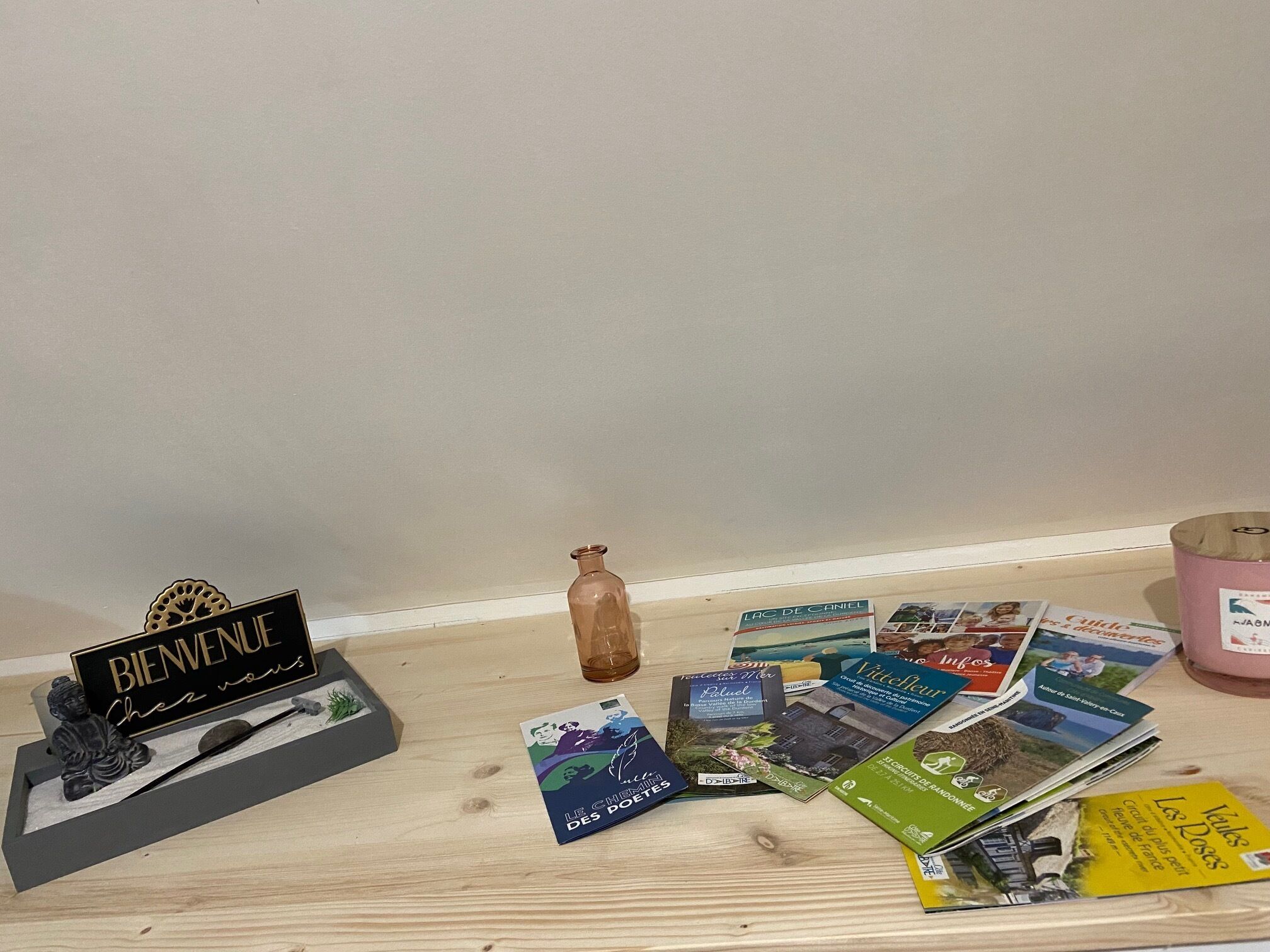 A wooden table with a welcome sign, a small Buddha statue, a glass bottle, and various brochures.