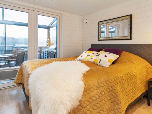 A bedroom with a large bed, a fluffy white throw, and a view of a balcony with outdoor furniture.