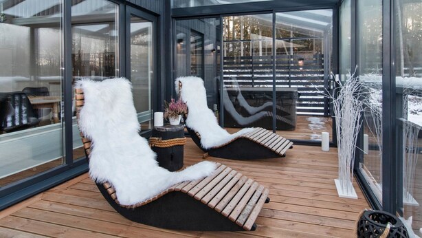 Ein moderner, ganzgläserner Lounge-Bereich mit zwei weißen, flauschigen Sesseln, einem kleinen Tisch mit einer Vase und Blick auf eine verschneite Landschaft.
