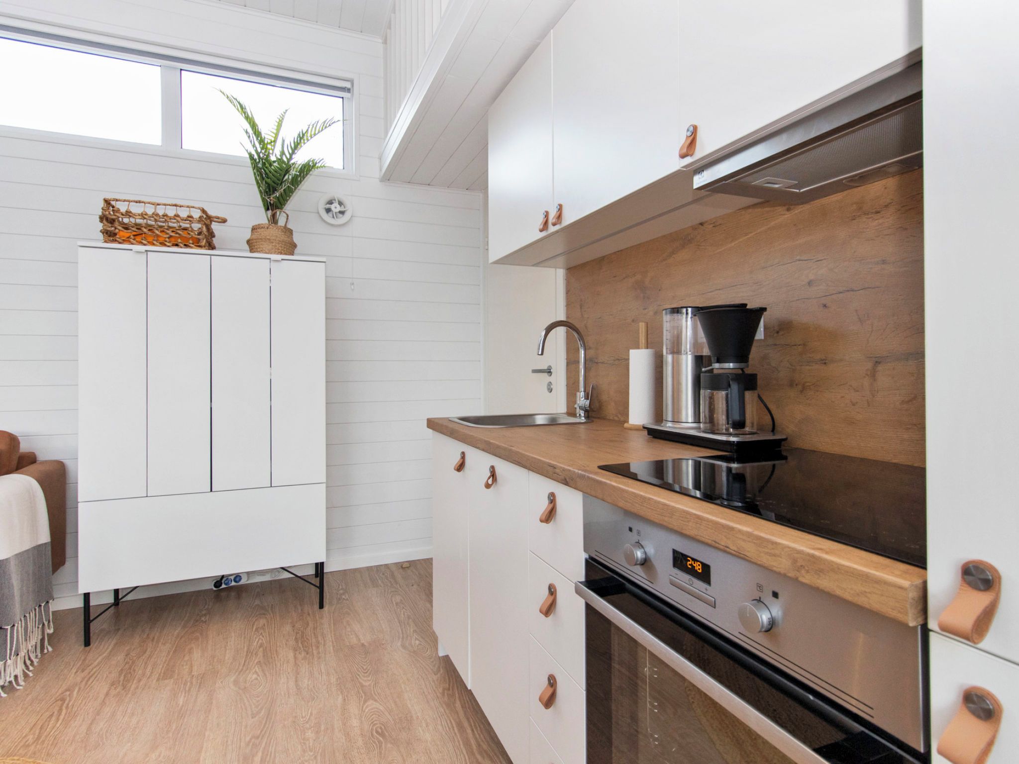 A modern kitchen with white cabinetry, a wooden countertop, a coffee maker, and a built-in oven.