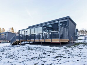 Een modern gebouw met een glazen gevel, een houten terras en metalen hekwerk.