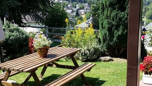 A wooden picnic table with potted plants in a garden area with a mountain view.