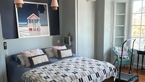 Een slaapkamer met een groot bed, een kroonluchter, een schilderij van een strandhuis en een houten vloer.