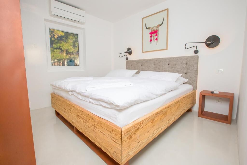 Un dormitorio moderno con una cama de madera, una ventana con vistas a árboles, una obra de arte colgada en la pared y una mesita de noche pequeña.
