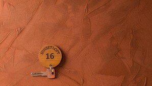 A wooden keychain with the text "SUNSET LOFT 16" on a textured orange background.