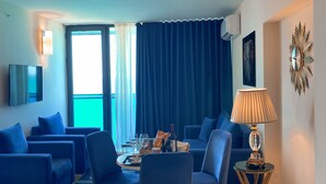 Een moderne woonkamer met blauwe banken, een eettafel met stoelen, een lamp en een televisie.