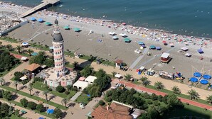 Luchtbeeld van een strand met een opvallende toren, veel parasols en een heldere lucht.