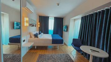A hotel room with a bed, a desk, a chair, a small table, and a TV.