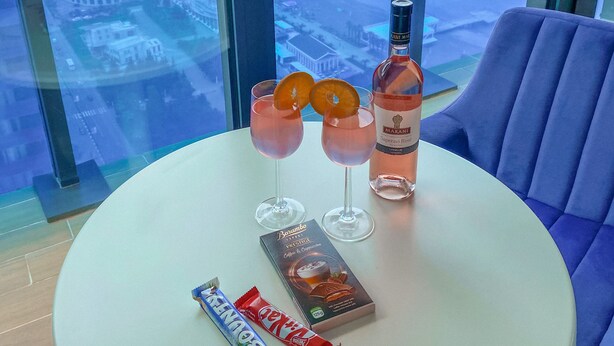 Een tafel met twee glazen roze drank, een fles Marani Superavi Rosé, en twee chocoladerepen op een balkon met uitzicht over de stad.