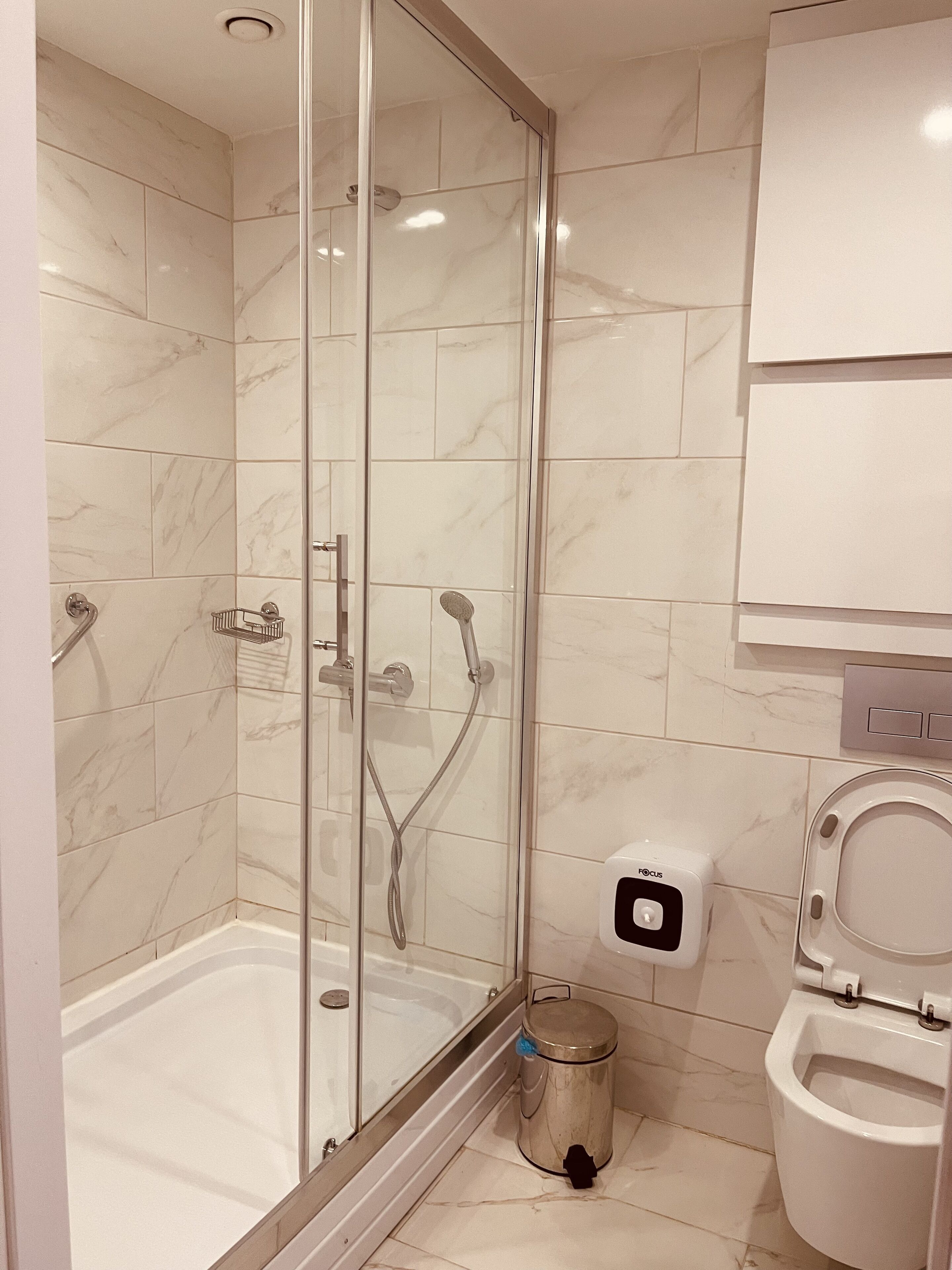 Un baño moderno con ducha de vidrio, inodoro y un cubo de basura.