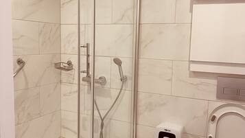 Un baño moderno con ducha de vidrio, inodoro y un cubo de basura.