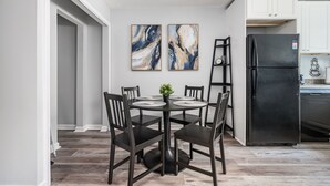 Eine moderne Küche mit weißen Schränken, einem schwarzen Kühlschrank und einem Essbereich mit rundem Tisch und Stühlen.