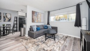 Ein modernes Wohnzimmer mit grauem Sofa, einem runden Couchtisch und einem Essbereich mit kleinem Tisch und Stühlen.