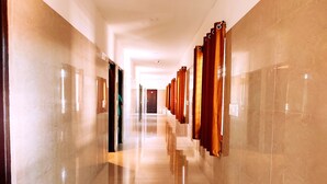 Un pasillo con paredes de mármol pulido y un suelo reflectante, que conduce a una puerta al final.