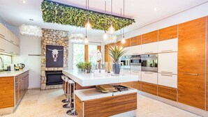 Una cocina moderna con una isla central, armarios de madera, un muro decorativo de piedra y lámparas colgantes.