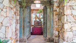 Un arco de piedra que da acceso a una habitación con alfombra roja, una lámpara colgante y un armario de madera.
