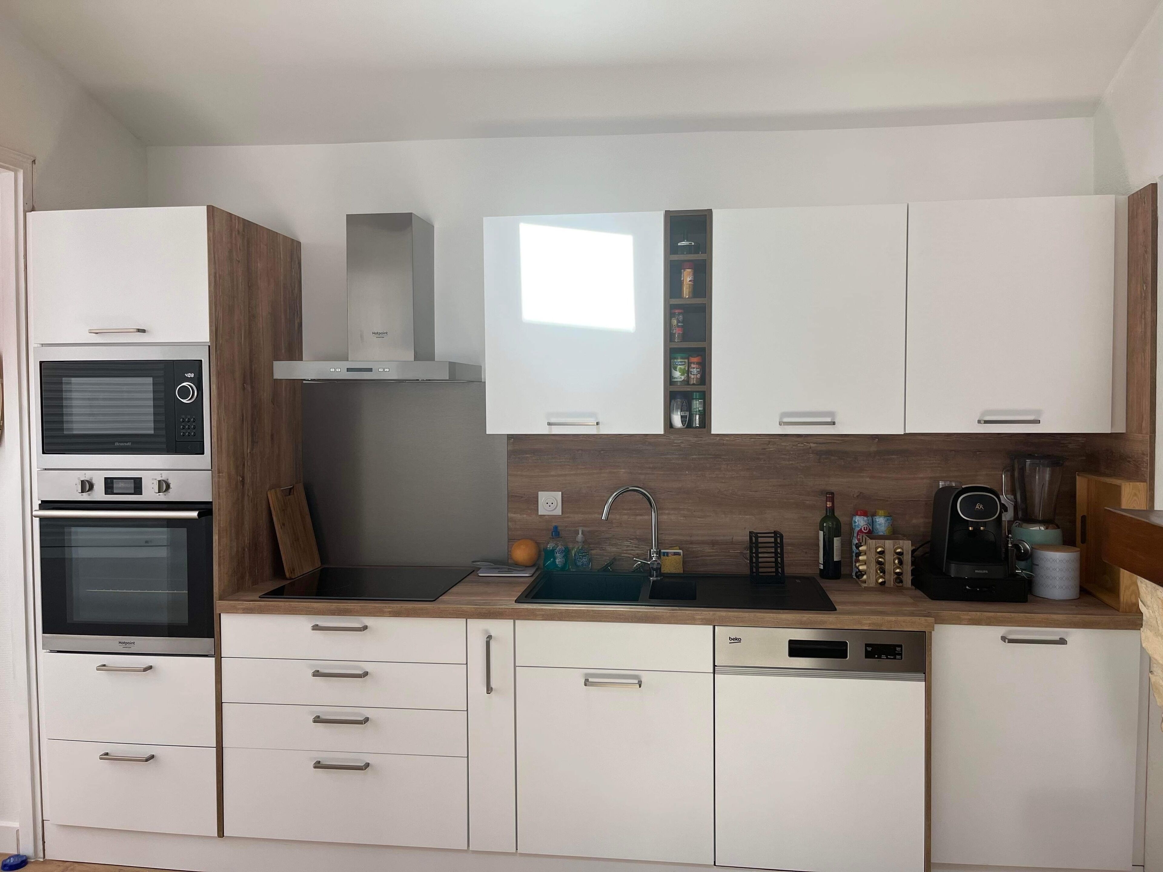 Una cocina moderna con armarios blancos, horno empotrado, microondas, pileta y cafetera.