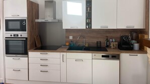 Eine moderne Küche mit weißen Schränken, einem eingebauten Backofen, einer Mikrowelle, einer Spüle und einer Kaffeemaschine.