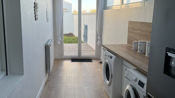 Eine moderne Küche mit eingebauter Waschmaschine und Trockner, einer Holzarbeitsplatte und Blick ins Freie durch eine Glastür.