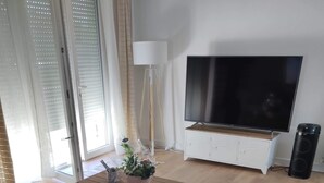 Ein modernes Wohnzimmer mit einer Couch, einem Couchtisch mit Dekoration, einem Fernseher auf einem Schrank und einer Stehlampe.