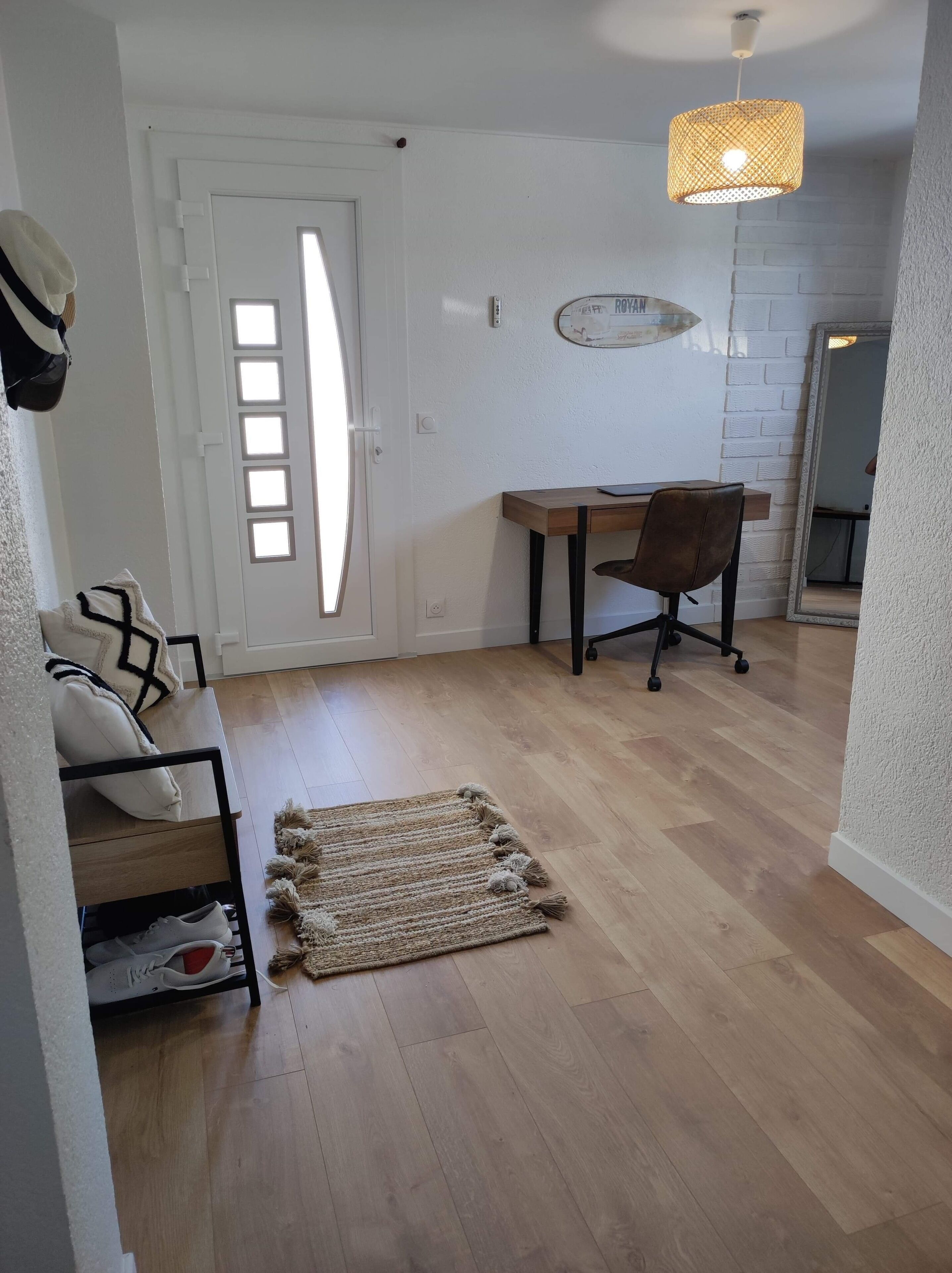 A modern interior with a wooden floor, a desk with a chair, a patterned rug, and a white door with a window.
