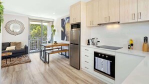 A modern kitchen with wooden cabinets, a stainless steel refrigerator, a built-in oven, and a dining area with a table and chairs. - 12 Calming Coral Beach Beautiful 2BRM (Scarborough)
